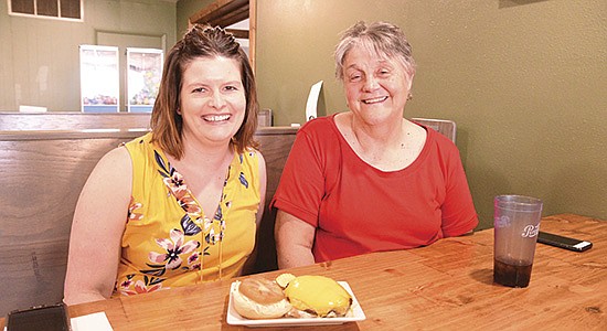 Hope Turner (left) and Karyl Diersen sit in a booth displaying a cheeseburger at Elsie’s Bar and Grill in Caledonia, Minnesota. The two women are board members for the Houston County American Dairy Association that worked with the local restaurant to pay for an extra slice of cheese on burgers throughout June.   PHOTO BY KRISTA KUZMA