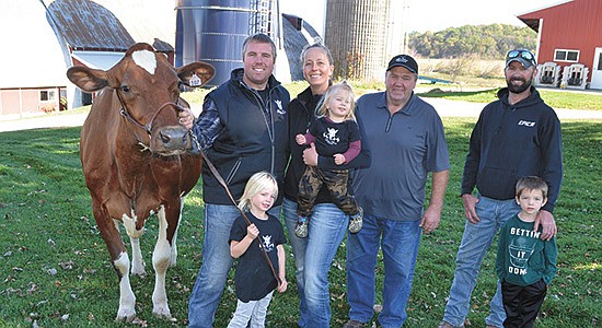 Members of Bert-Mar Farms – (from left) Erica Lundberg’s fiancé, Grahm Giese, Loveiisa Mackey, Erica Lundberg holding Aksel Mackey, Allan Lundberg, in-house breeder Ryan Nordahl and James Nordahl – pose with Josey LLC Duc Saber-Red EX94, one of their elite cows, on their farm near Osseo, Wisconsin. The Lundbergs are rebuilding their herd after suffering from years of stray voltage. The Mackeys are Allan Lundberg’s grandkids.  PHOTO BY ABBY WIEDMEYER