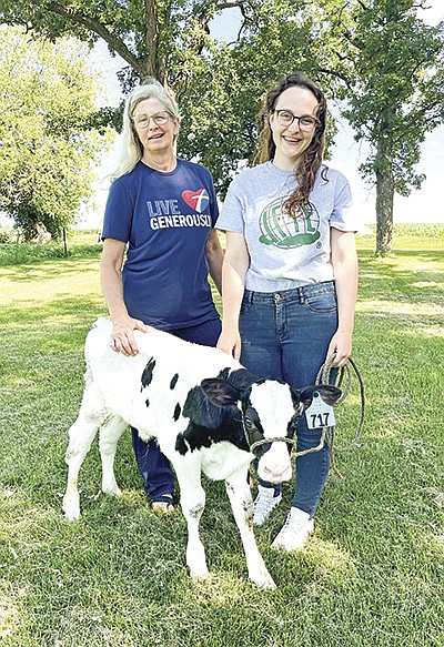 Natalie Schmitt and Julia Kolb stand with a calf on the Schmitts’ dairy farm July 10 in rural Rice, Minnesota. Kolb is a part of the International Farming Youth Exchange program, and the Schmitts are one of the four host families she will be staying with this summer.  PHOTO BY MAGGIE MOLITOR