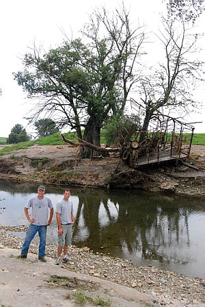 Chad and Brent Koopmann stand next to the stream that turned into a raging torrent the early morning hours of July 28 on their farm near Epworth, Iowa. The Koopmanns lost several pieces of farm equipment they were no longer using, including the hay wagon now in the tree on the other side of the stream. (photo by Kelli Boylen)